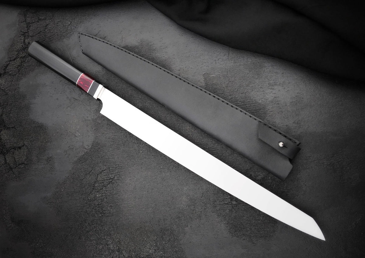 Brisket cutting knife with long polished blade and red and black resin handle beside leather sheath

