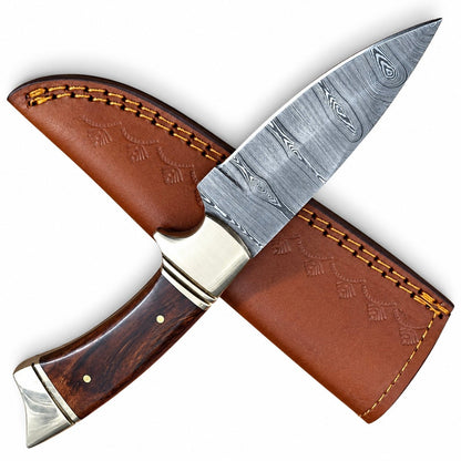 Drop point skinning knife resting on its tooled leather sheath