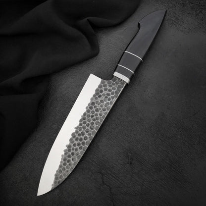 Hammered kitchen chef knife with polished edge and black Micarta handle on dark surface
