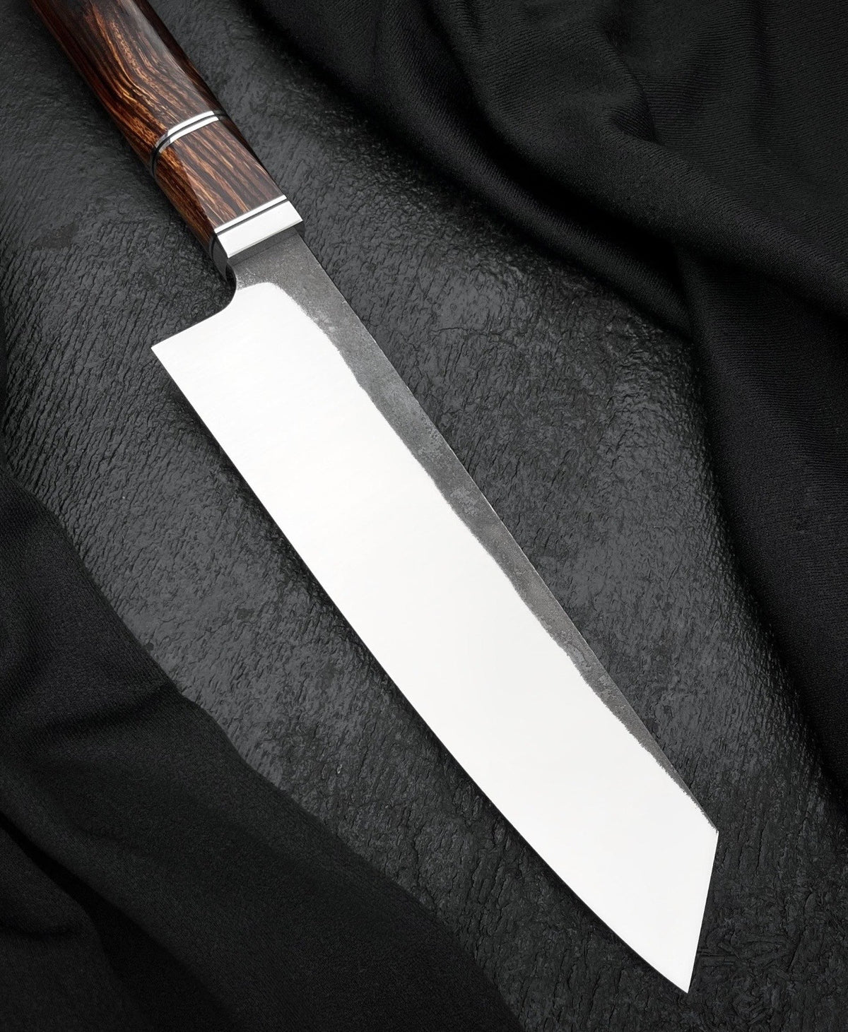 Handmade 8 inch kitchen knife with flat edge and dark textured finish near the heel
