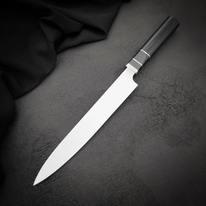 Handmade 9 inch sushi slicer with straight spine and pointed tip beside black fabric
