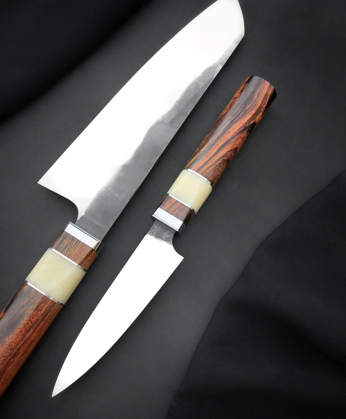 Handmade chef knife with angled tip and small paring knife with pointed tip laid side by side
