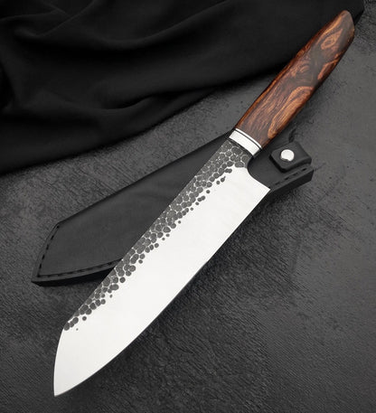 Chef knife with sheath showing hammered santoku blade and swirled brown wood handle on dark surface
