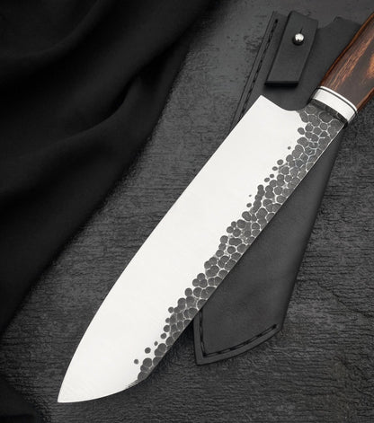 Black stitched leather knife sheath with snap strap beside a chef knife
