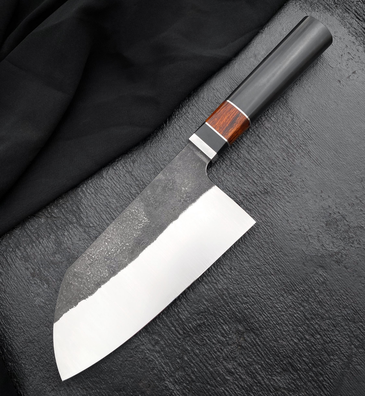 Bunka chef knife with angled tip, dark upper blade and black octagonal Micarta and wood handle
