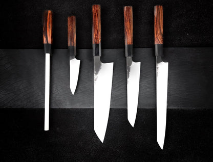 Wood handle knife set with four kitchen knives and a honing rod laid out in a row on black
