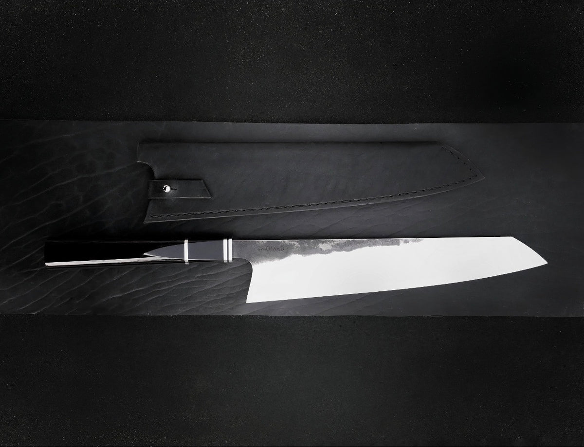Kiritsuke knife with polished 10 inch blade and black octagonal resin handle beside leather sheath
