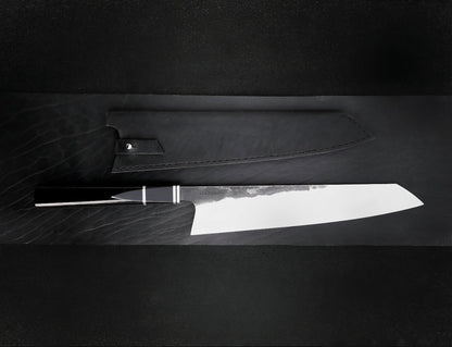 Kiritsuke knife with polished 10 inch blade and black octagonal resin handle beside leather sheath
