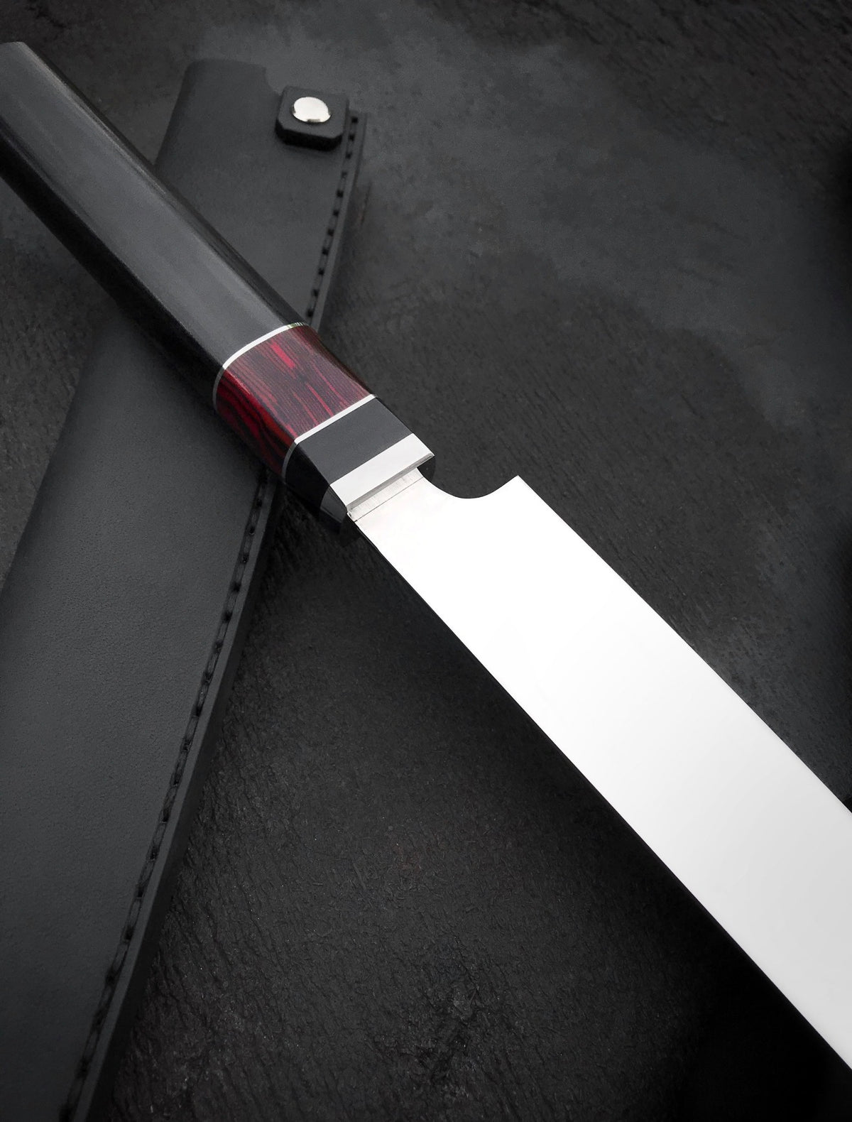 Long stainless steel slicing knife with resin and bone handle next to black fabric
