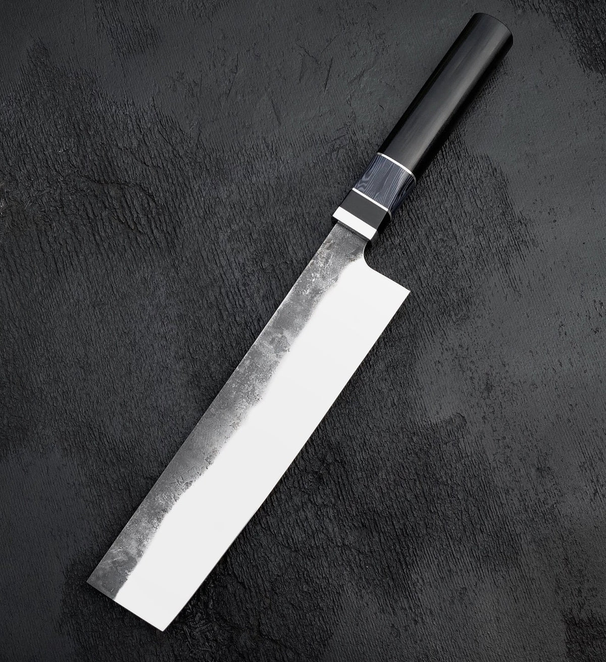 Nakiri vegetable knife with rectangular polished blade and black Micarta and wood handle on dark surface
