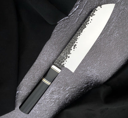 Santoku blade kitchen cooking knife with hammered 440C blade and black Micarta handle on gray textured surface
